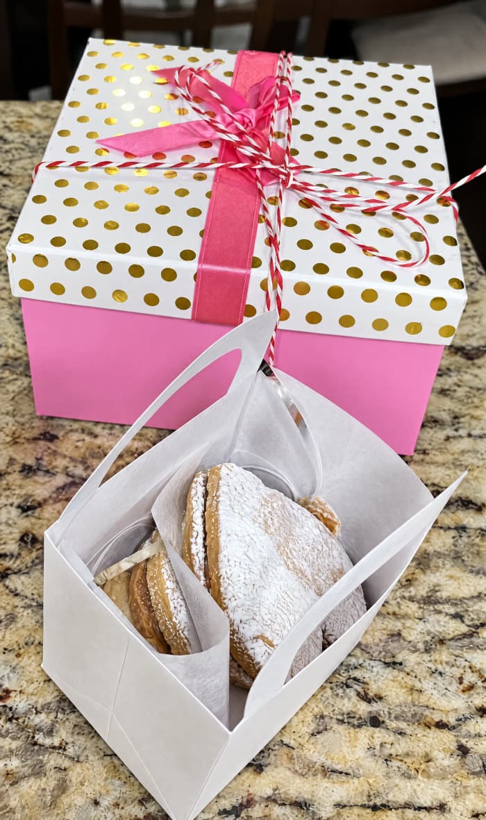 A pink polka-dot gift box tied with ribbon, filled with alfajores